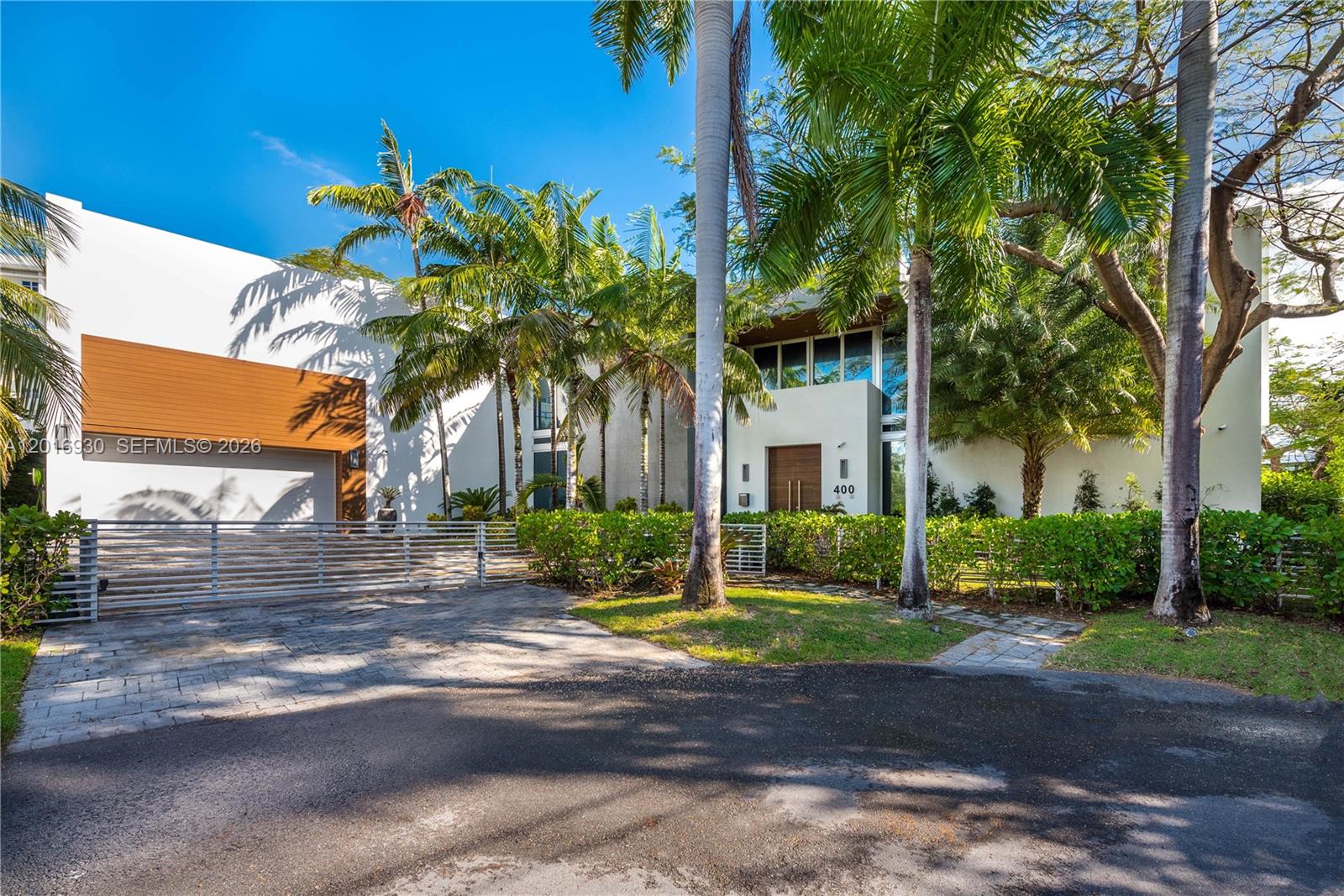 A modern two-story house features a white exterior, wood accents, a gated driveway, and palm trees — 400 Tamarind Dr, Hallandale Beach FL 33009, HALLANDALE BEACH, FL