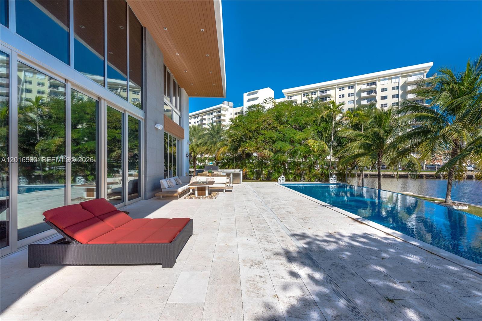 A modern patio features a red lounge chair, outdoor seating, and an infinity pool overlooking water — 400 Tamarind Dr, Hallandale Beach FL 33009, HALLANDALE BEACH, FL