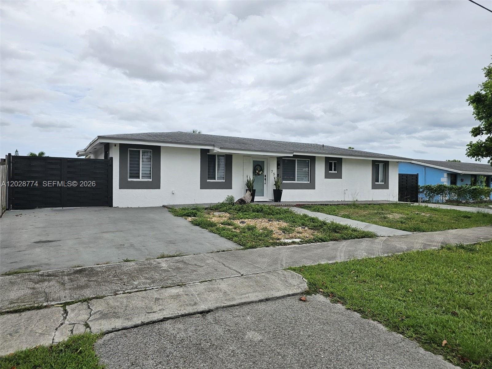 A single-story white house with gray trim features a concrete driveway and a front lawn — 75 SW 18th Ave, Homestead FL 33030, HOMESTEAD, FL