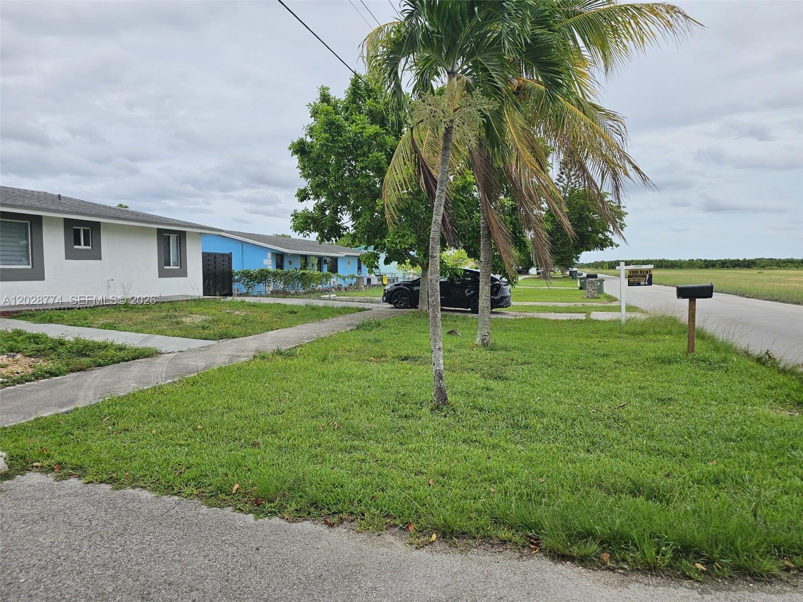 A single-story house with a blue exterior sits next to a grassy field — 75 SW 18th Ave, Homestead FL 33030, HOMESTEAD, FL