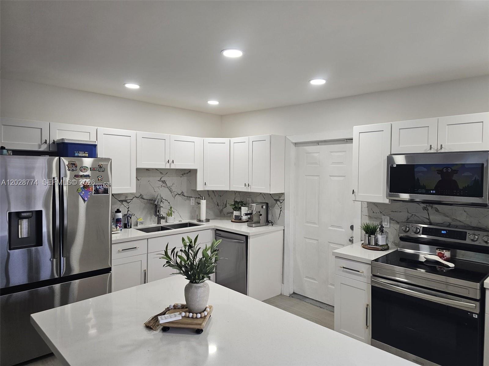 A modern kitchen features white cabinets, stainless steel appliances, and a marble-patterned backsplash — 75 SW 18th Ave, Homestead FL 33030, HOMESTEAD, FL