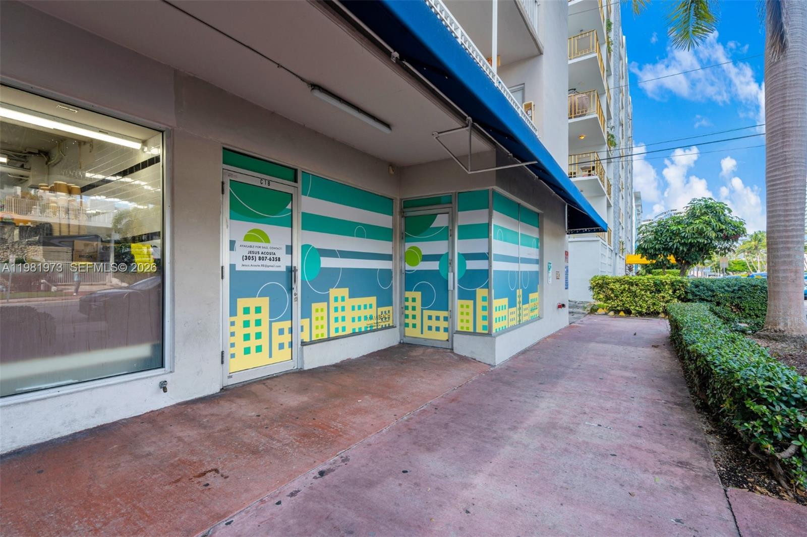 The exterior of a commercial storefront features blue and green window decals and a blue awning — 1300 Lincoln Rd # 1B, Miami Beach FL 33139, MIAMI BEACH, FL