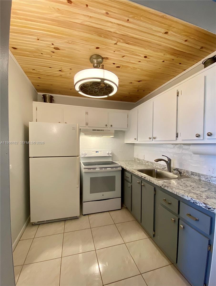 A kitchen features white upper cabinets, gray lower cabinets, granite countertops, and a wood-paneled ceiling — 142 Preston D # 142, Boca Raton FL 33434, BOCA RATON, FL
