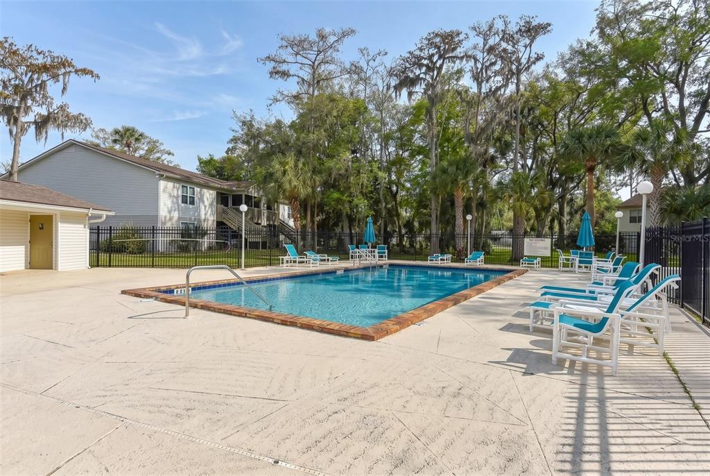 An outdoor swimming pool surrounded by lounge chairs, a black fence, and trees — 1600 BIG TREE ROAD UNIT G3, SOUTH DAYTONA, FL