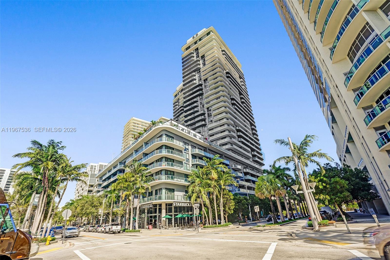 A low-angle exterior view of a modern high-rise building with a street-level Starbucks — 121 NE 34th St # 1705, Miami FL 33137, MIAMI, FL