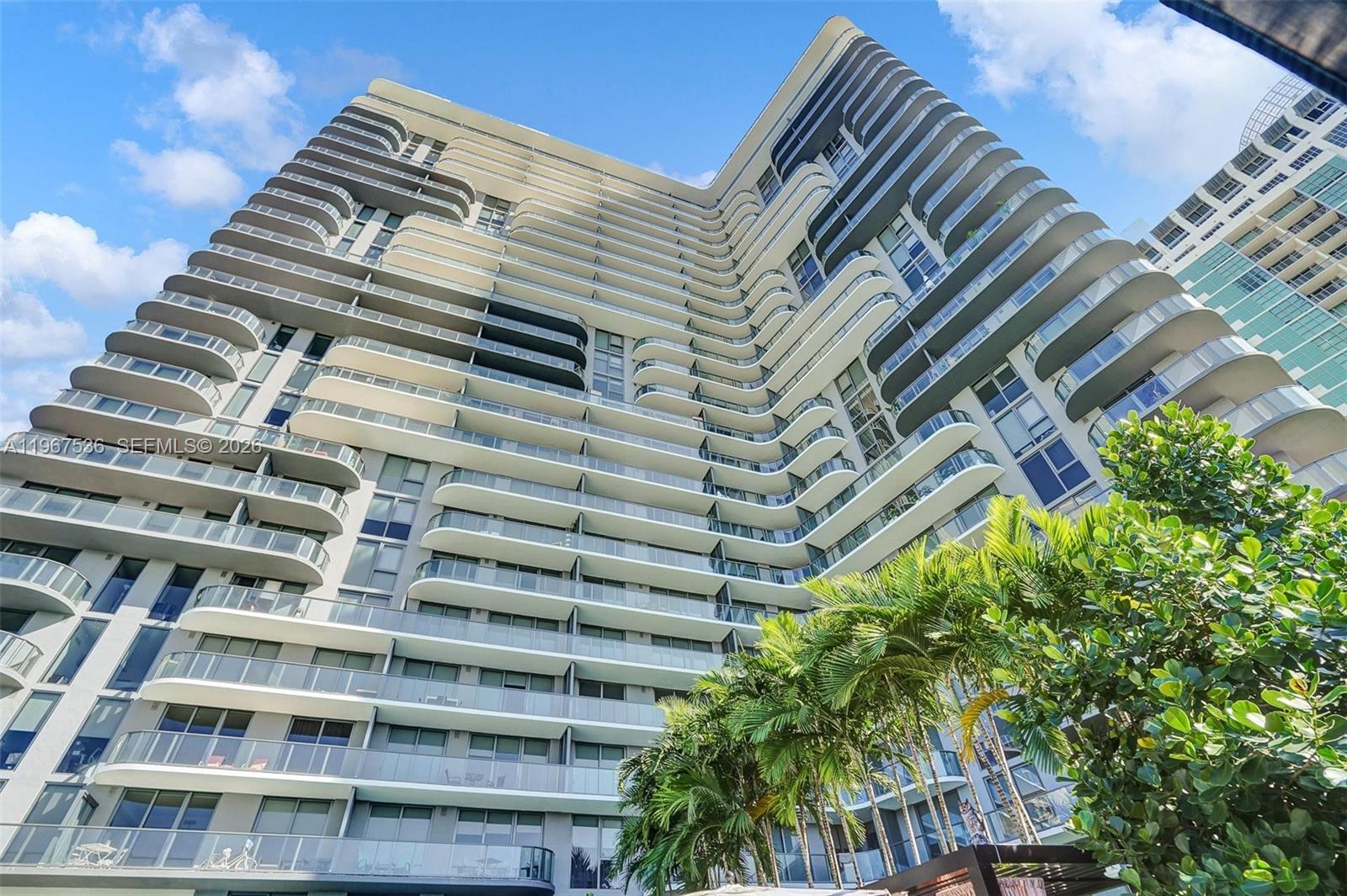 A low-angle view shows the exterior of a modern high-rise building with curved balconies — 121 NE 34th St # 1705, Miami FL 33137, MIAMI, FL