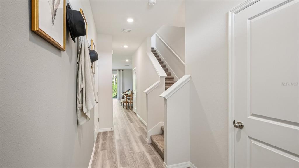 A hallway with light wood-look flooring leads to a dining area past a carpeted staircase — 32451 WELLING BLADE LOOP, WESLEY CHAPEL, FL