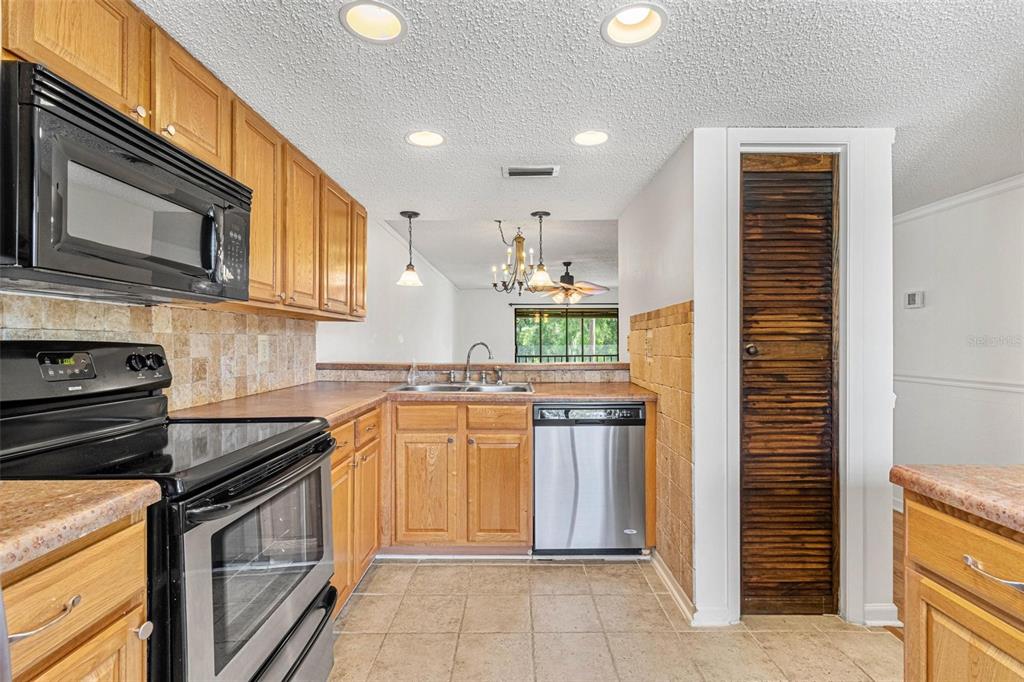 A kitchen with wood cabinets, stainless steel appliances, tile backsplash, and a louvered pantry door — 108 WOODLANDS COURT UNIT 108, OLDSMAR, FL
