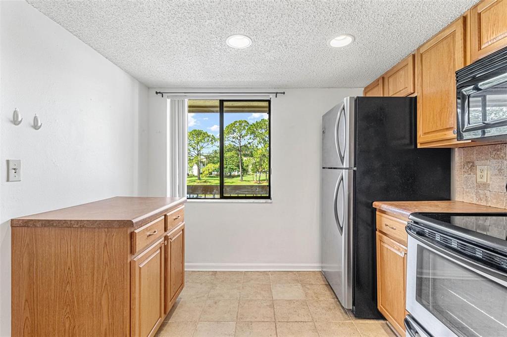 A kitchen features wooden cabinets, a black refrigerator, a stove, and a window with outdoor views — 108 WOODLANDS COURT UNIT 108, OLDSMAR, FL