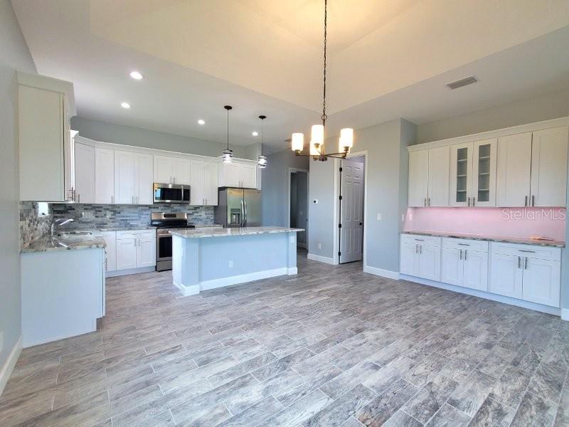 A kitchen features white cabinetry, a central island, stainless steel appliances, and wood-look tile flooring — 1038 SAN CRISTOBAL AVENUE, PUNTA GORDA, FL