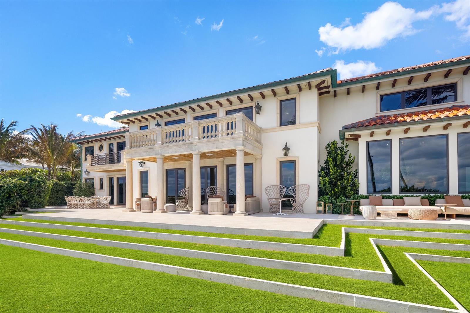 The exterior of a large Mediterranean-style house features a stone patio and tiered grass lawn — 680 S Ocean Boulevard, Palm Beach FL 33480, PALM BEACH, FL
