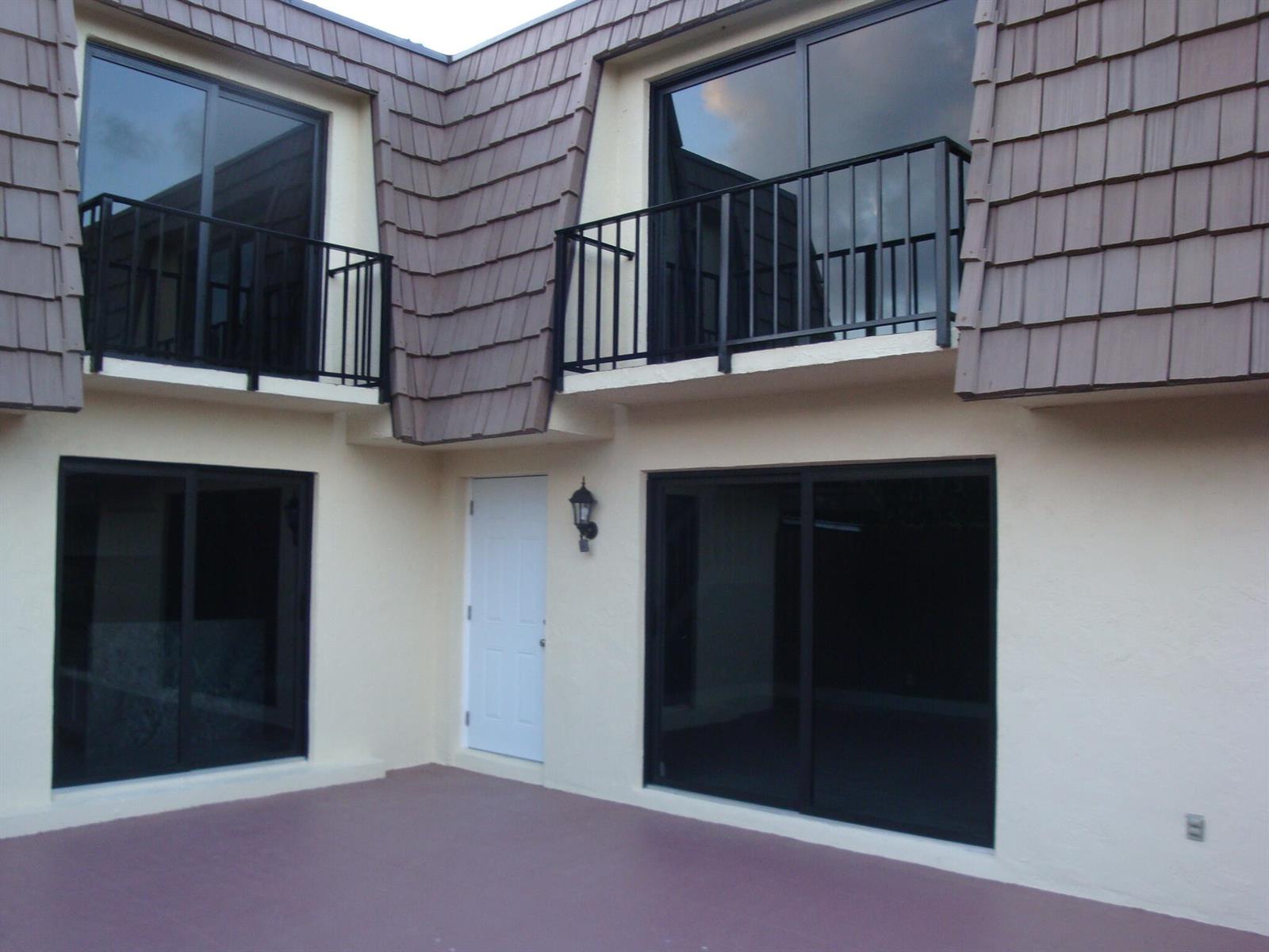 Exterior view of a two-story building with a patio, sliding glass doors, and balconies — 594 Springdale Circle # d, Palm Springs FL 33461, PALM SPRINGS, FL