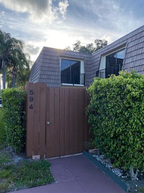 A brown wooden gate and fence stand before a two-story building with a mansard roof — 594 Springdale Circle # d, Palm Springs FL 33461, PALM SPRINGS, FL