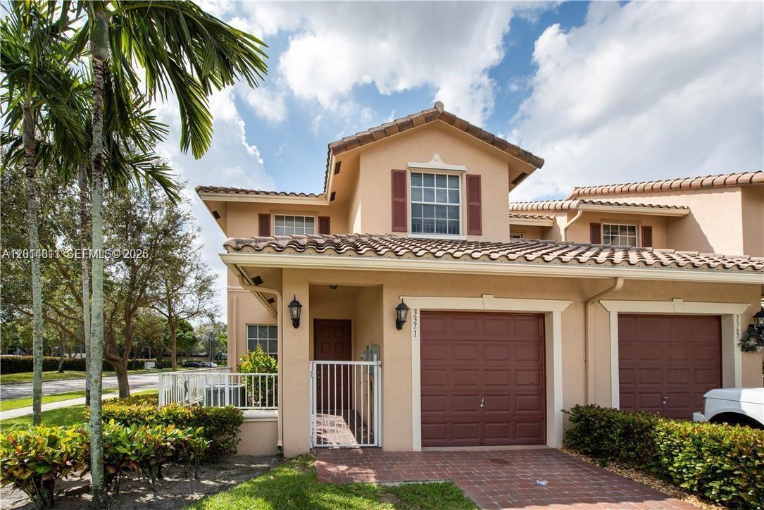 A two-story townhouse features a tan stucco exterior, a brown garage door, and a tiled roof — 3371 Lakeside Dr # 27, Davie FL 33328, DAVIE, FL