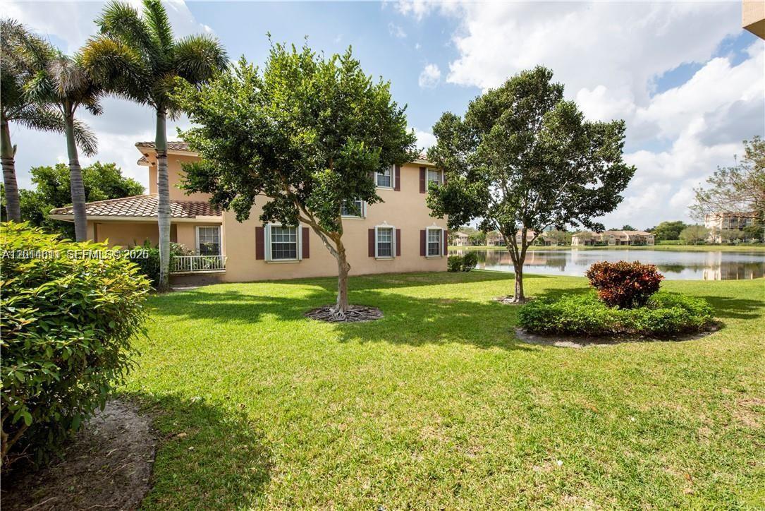 A two-story tan house sits on a grassy lawn beside a lake with trees — 3371 Lakeside Dr # 27, Davie FL 33328, DAVIE, FL