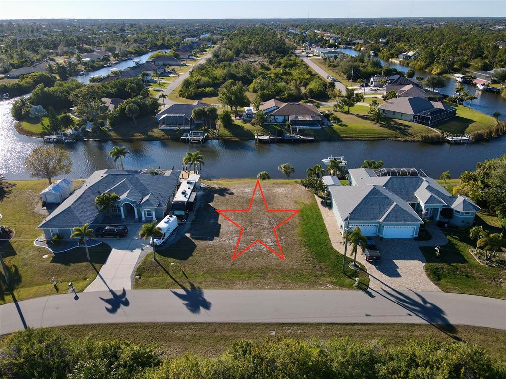 An aerial view shows a vacant waterfront residential lot situated between two existing houses — 15666 APPLEWHITE CIRCLE, PORT CHARLOTTE, FL