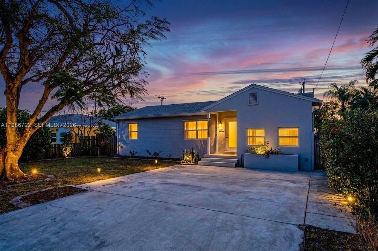 A single-story house with a concrete driveway, a large tree, and exterior lighting at dusk — 1508 Funston St, Hollywood FL 33020, HOLLYWOOD, FL
