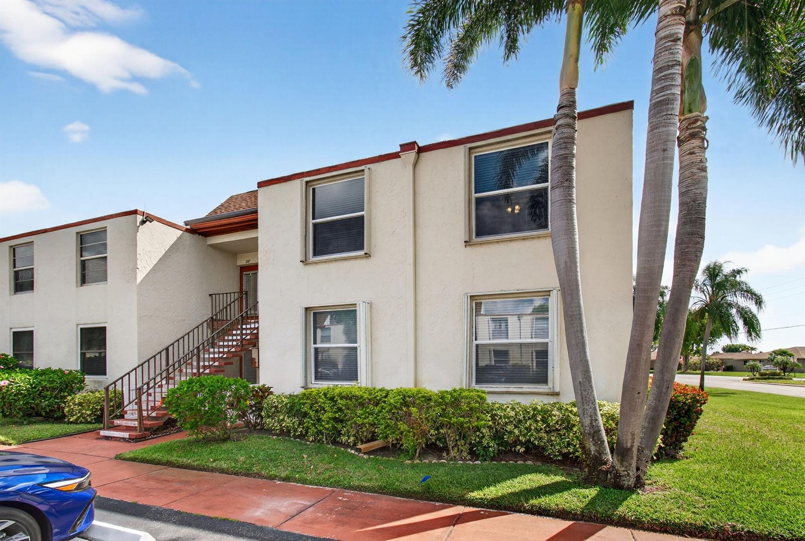 A two-story apartment building with beige stucco walls, brown trim, and an exterior staircase — 9 Willowbrook Lane # 208, Delray Beach FL 33446, DELRAY BEACH, FL