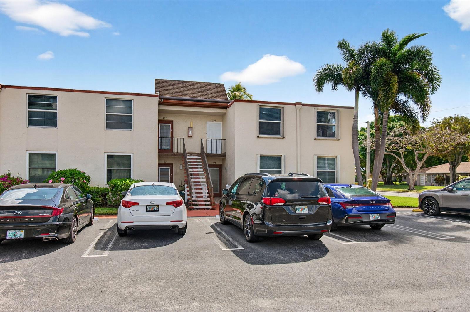 A two-story apartment building exterior with a central staircase and four parked cars — 9 Willowbrook Lane # 208, Delray Beach FL 33446, DELRAY BEACH, FL