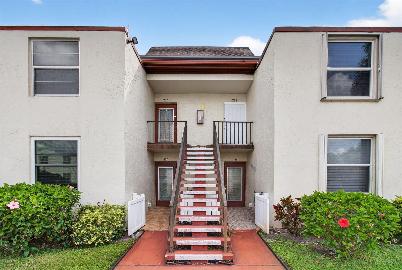 A two-story apartment building exterior features a central staircase leading to upper-level units — 9 Willowbrook Lane # 208, Delray Beach FL 33446, DELRAY BEACH, FL