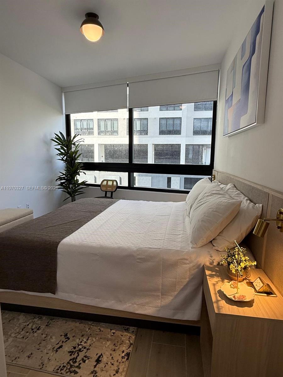 A bedroom features a bed, a nightstand with a lamp, and a window overlooking buildings — 225 N Miami Ave # 804, Miami FL 33128, MIAMI, FL