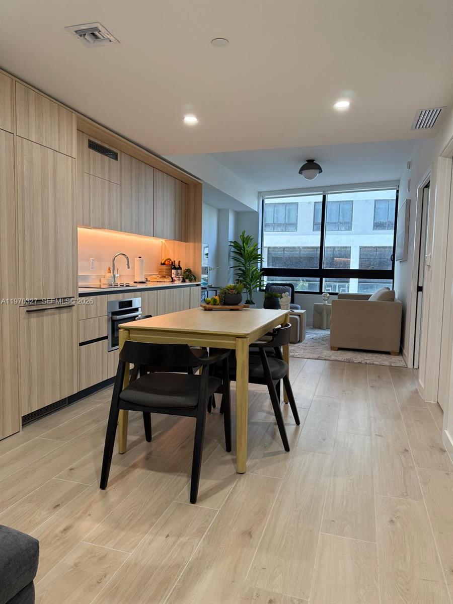 A modern kitchen with light wood cabinetry and a dining table sits before a living area — 225 N Miami Ave # 804, Miami FL 33128, MIAMI, FL
