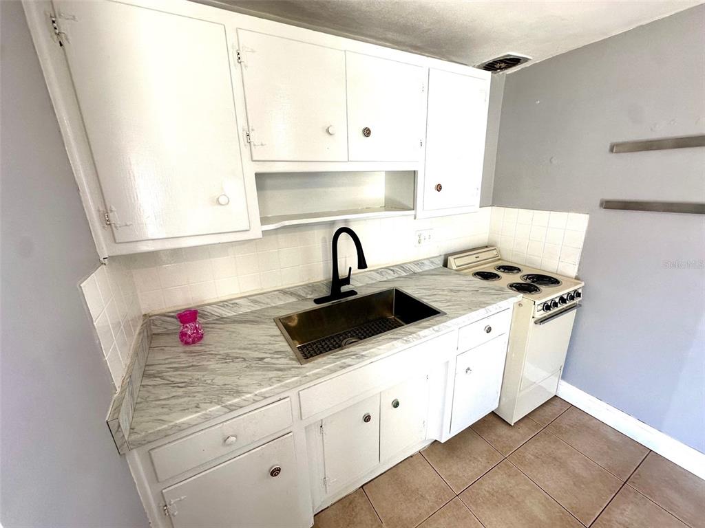 A small kitchen features white cabinets, a marble-patterned countertop, a stainless sink, and a stove — 2035 EDGEWATER DRIVE UNIT 10, CLEARWATER, FL