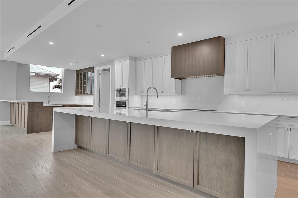 A modern kitchen features a large white-topped island, wood-toned cabinetry, and white upper cabinets — 70 AVENIDA VENECCIA UNIT 304, SARASOTA, FL