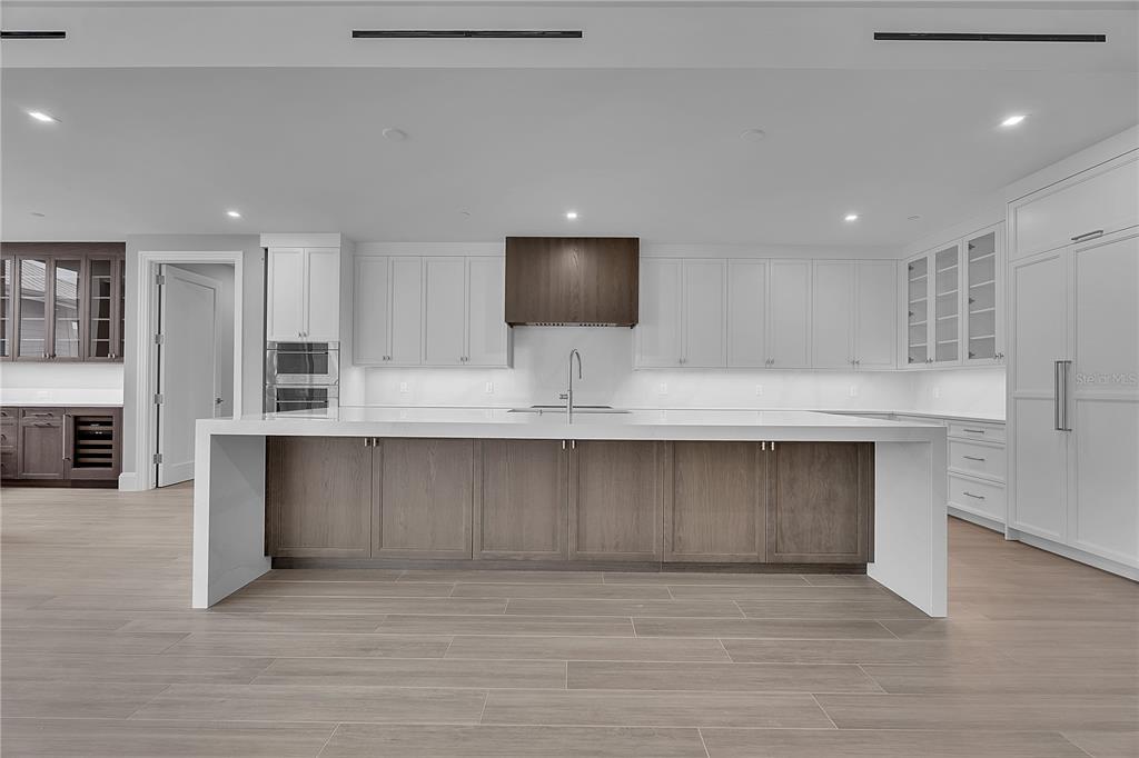 A modern kitchen features white cabinetry, a large two-toned island, and light wood-look flooring — 70 AVENIDA VENECCIA UNIT 304, SARASOTA, FL