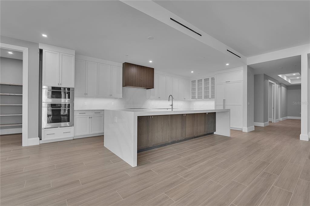 A modern kitchen features white cabinetry, a large central island with wood paneling, and appliances — 70 AVENIDA VENECCIA UNIT 304, SARASOTA, FL