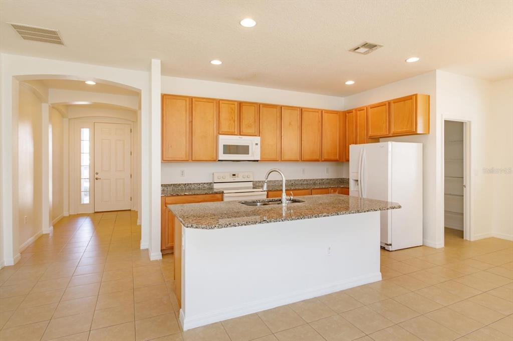 A kitchen with light wood cabinets, granite countertops, a center island, and white appliances — 339 MARIVAL DRIVE, DAVENPORT, FL