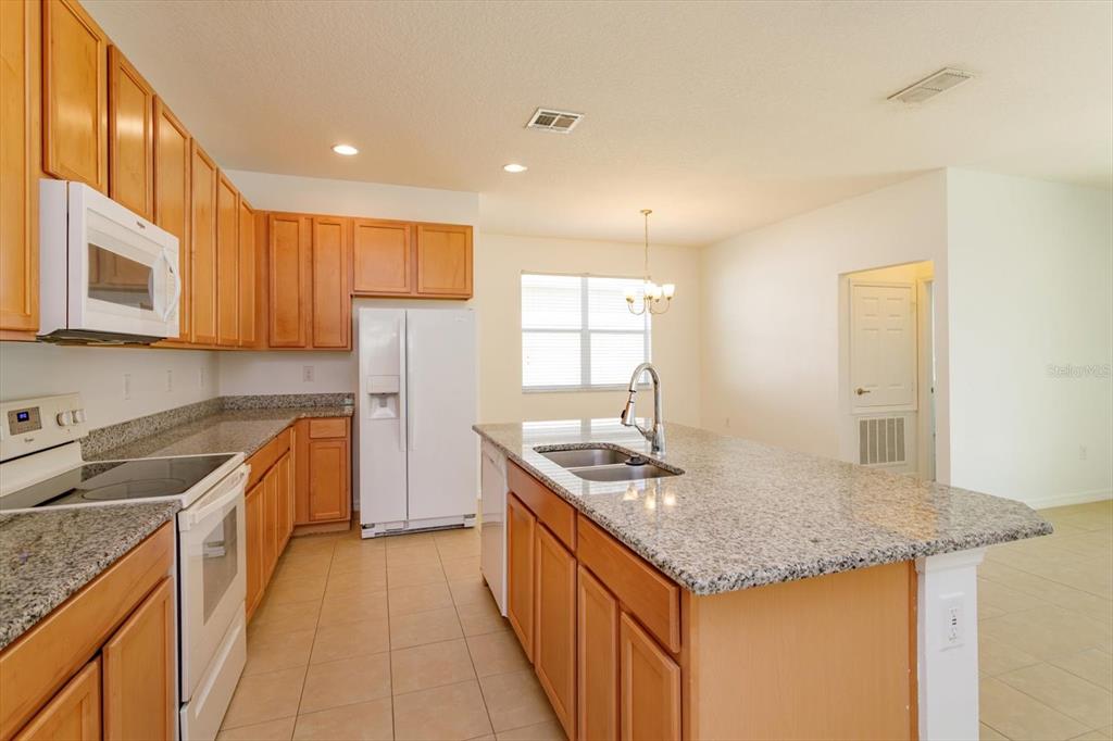 A kitchen with light wood cabinets, granite countertops, an island, and white appliances — 339 MARIVAL DRIVE, DAVENPORT, FL