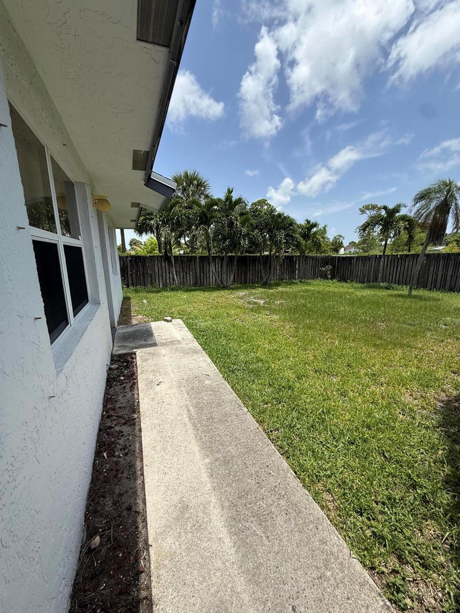 A concrete walkway runs along the side of a white house toward a grassy backyard — 3961 Park Lane # B, Palm Springs FL 33406, PALM SPRINGS, FL