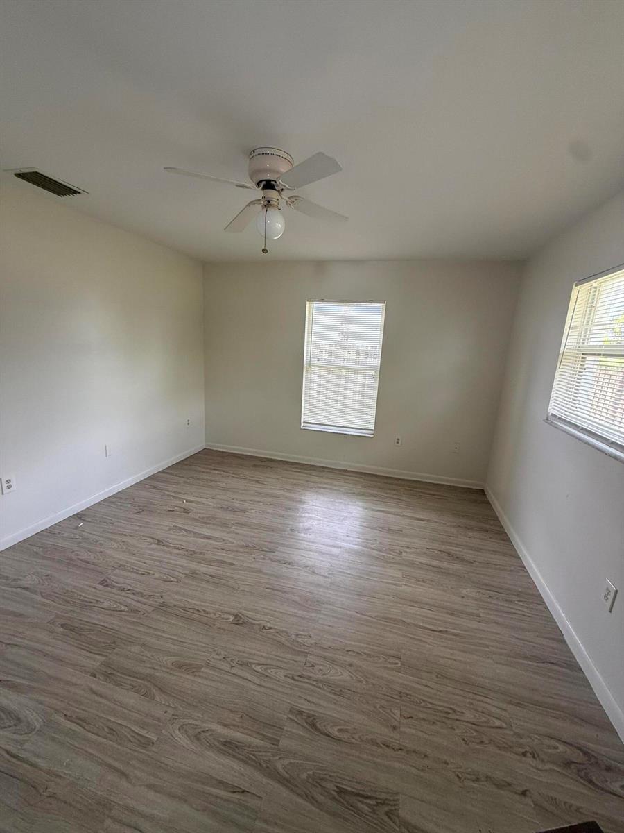 An empty bedroom features light-colored walls, wood-look flooring, a ceiling fan, and two windows — 3961 Park Lane # B, Palm Springs FL 33406, PALM SPRINGS, FL