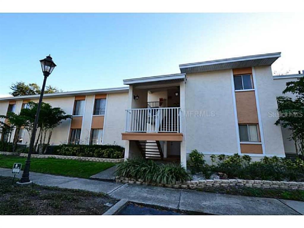 A two-story apartment building exterior features white stucco walls, brown accents, and a central balcony — 720 100TH AVENUE N UNIT 203, ST PETERSBURG, FL