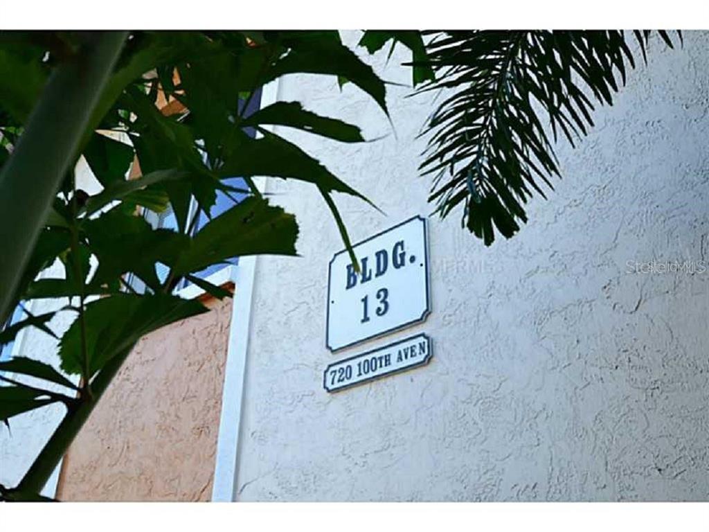 A building identification sign labeled 13 and 720 100th Aven is mounted on a stucco wall — 720 100TH AVENUE N UNIT 203, ST PETERSBURG, FL