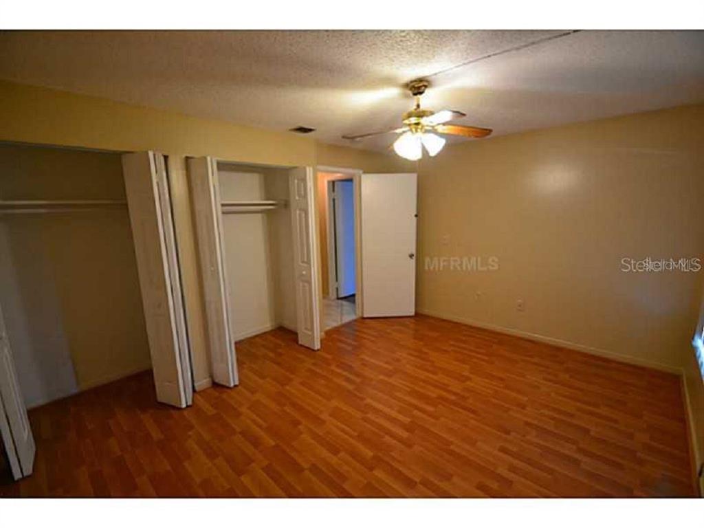 A bedroom features light-colored walls, wood-look flooring, a ceiling fan, and open closet doors — 720 100TH AVENUE N UNIT 203, ST PETERSBURG, FL