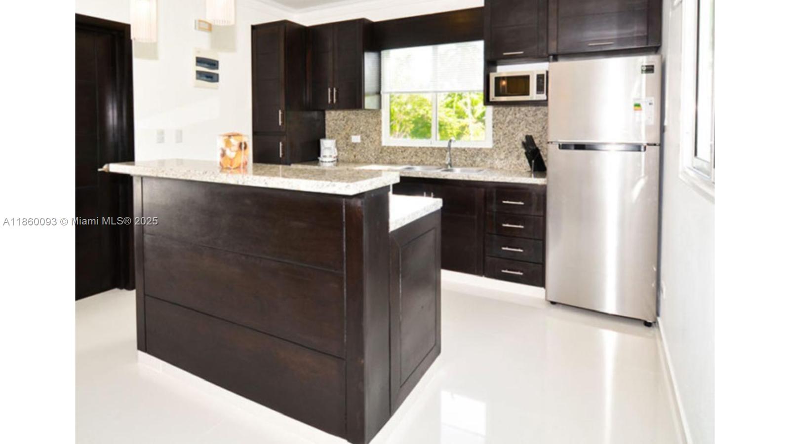 A kitchen features dark wood cabinetry, granite countertops, stainless steel appliances, and white tile flooring — Los Corales Los Corales # 101, La, La