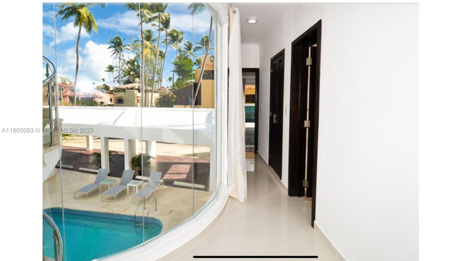 A hallway with dark doors overlooks a swimming pool through a large curved glass wall — Los Corales Los Corales # 101, La, La