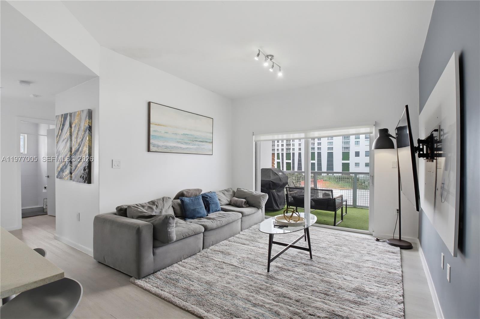 A living room features a gray sectional sofa, a glass coffee table, and a balcony — 481 NE 29th St # 604, Miami FL 33137, MIAMI, FL