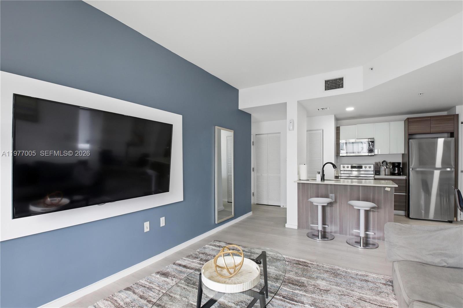 A living room with a blue accent wall, wall-mounted television, and an adjacent kitchen — 481 NE 29th St # 604, Miami FL 33137, MIAMI, FL