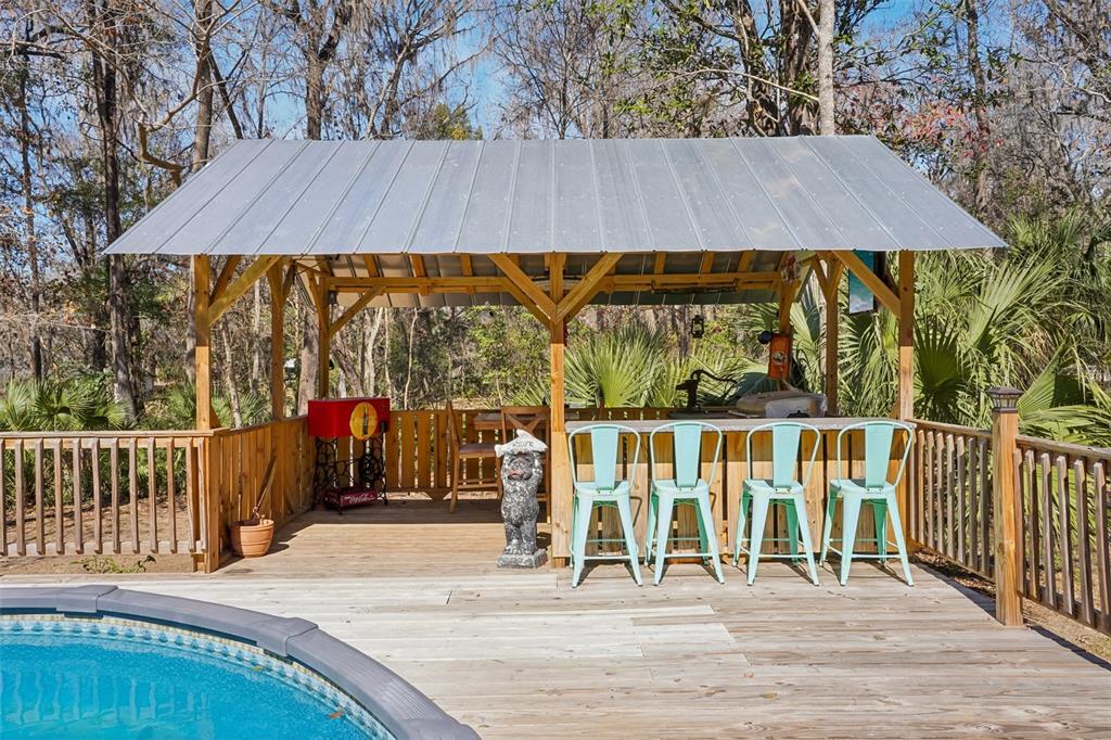 A wooden deck features a covered outdoor bar area with four teal metal stools — 7459 SW 5TH AVENUE, OCALA, FL