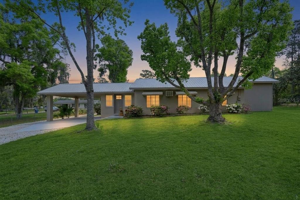 A single-story house with a metal roof, attached carport, and large trees in the yard — 4611 GRAND AVENUE, DE LEON SPRINGS, FL