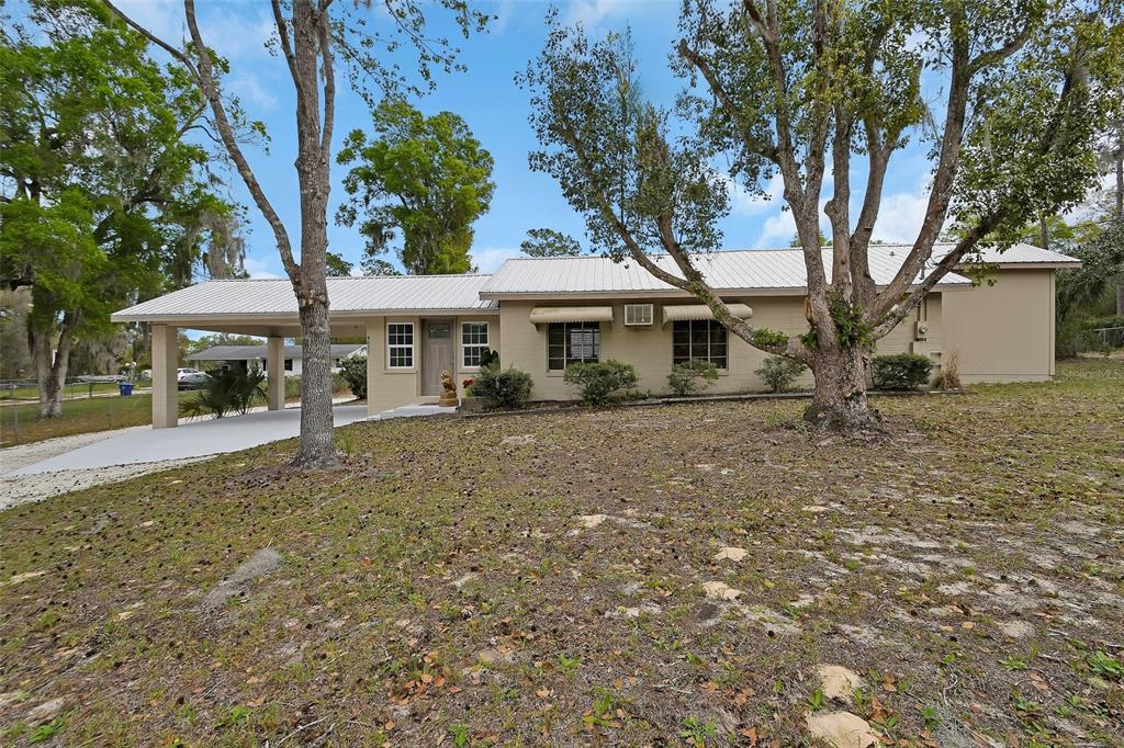 A single-story house with a metal roof, carport, and large trees in the front yard — 4611 GRAND AVENUE, DE LEON SPRINGS, FL