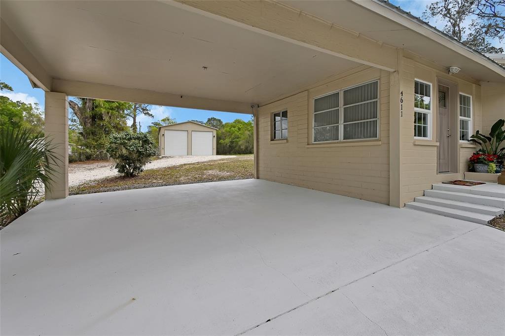 A beige house features a concrete carport and a detached two-car garage in the background — 4611 GRAND AVENUE, DE LEON SPRINGS, FL