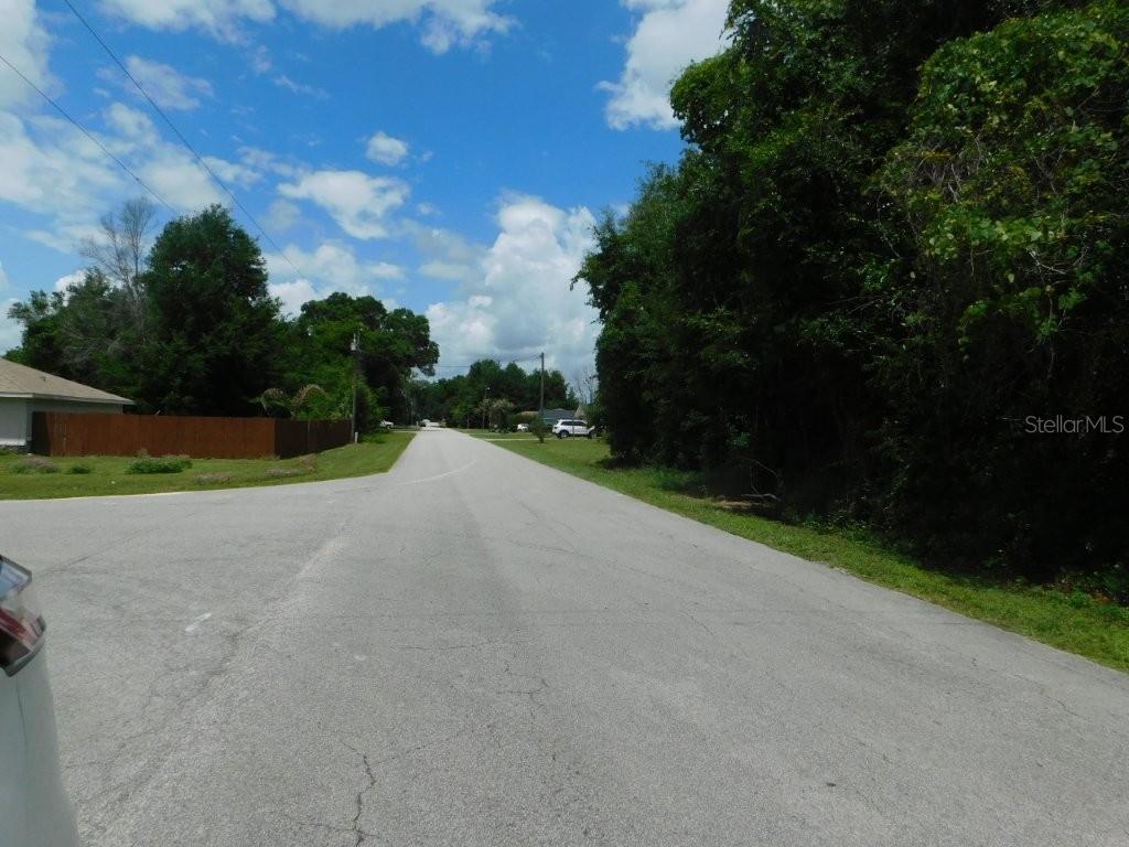 A paved residential street stretches into the distance between a wooden fence and trees — 0 NW 66TH STREET, OCALA, FL