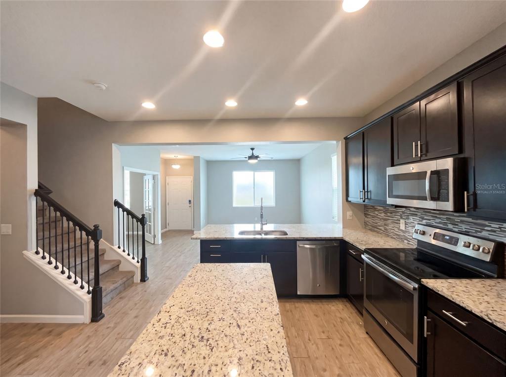 A kitchen with dark cabinets, granite countertops, stainless steel appliances, and an island — 2264 FICUS ALLEY, APOPKA, FL