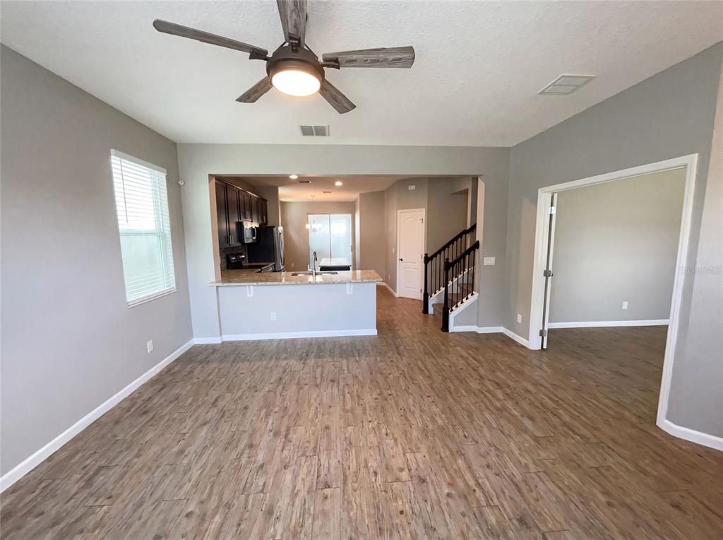 An open-concept living area features wood-look flooring, a ceiling fan, and a kitchen pass-through — 2264 FICUS ALLEY, APOPKA, FL