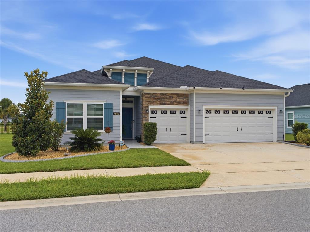 A single-story house with light blue siding, a stone accent wall, and a three-car garage — 7680 SW 74TH LOOP, OCALA, FL