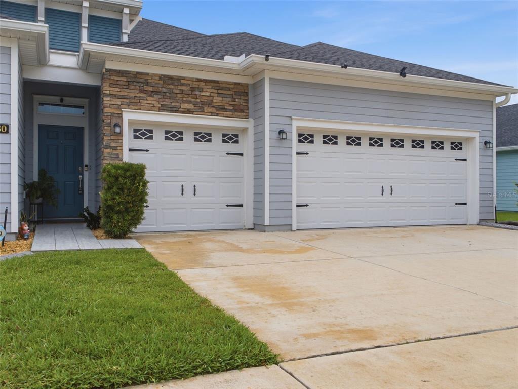 A front view of a house with a blue door, stone accents, and a three-car garage — 7680 SW 74TH LOOP, OCALA, FL